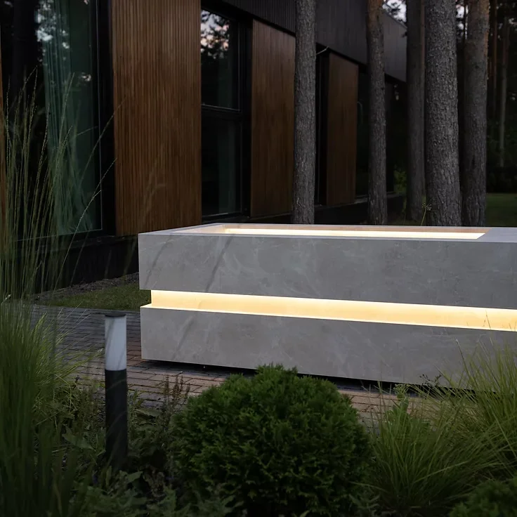 Banheira de imersão Nordic Vitality em pedra cinzenta com iluminação LED, num jardim ao anoitecer