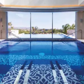 Piscina exterior junto a terraço com espreguiçadeiras, lustres decorativos e parede vegetal