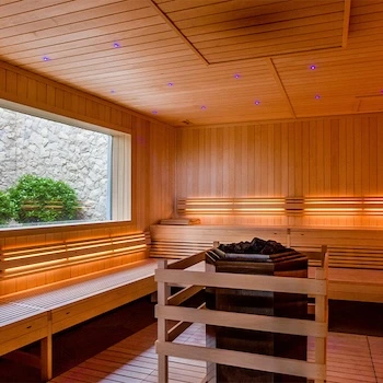 Sauna interior em painéis de madeira com bancos largos e iluminação ambiente relaxante