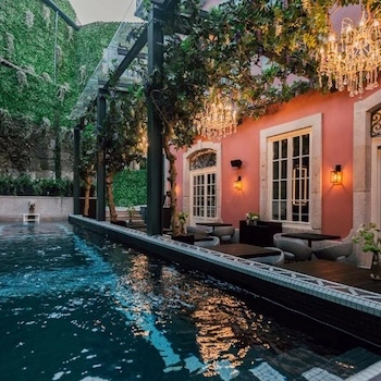 Piscina exterior junto a terraço com espreguiçadeiras, lustres decorativos e parede vegetal