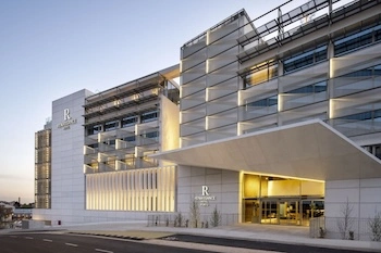 Fachada e entrada principal do hotel com cobertura moderna e iluminação suave ao pôr do sol