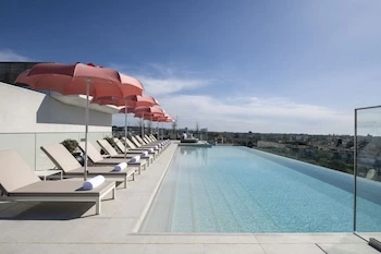 Piscina rooftop infinity com espreguiçadeiras e guarda-sóis cor-de-rosa, vista panorâmica sobre a cidade